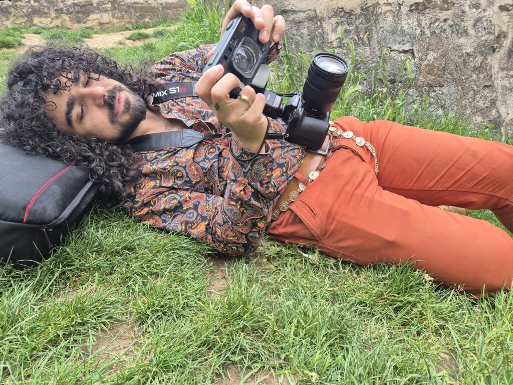 portrait du photographe Kevin Nicolini, allongé dans l'herbe, avec un appareil photo argentique à la main