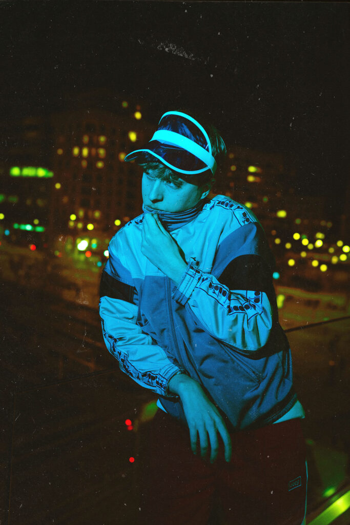 Portrait nocturne d’un jeune homme éclairé par un néon bleu, avec les lumières de la ville en arrière-plan