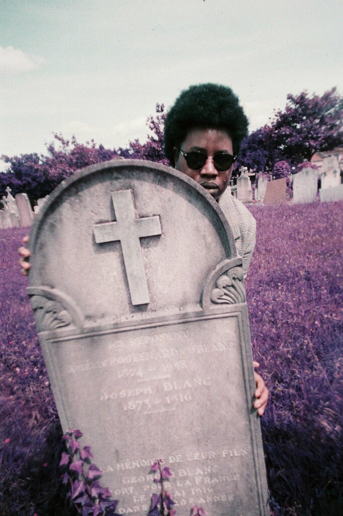 Portrait vintage psychédélique d'une femme noire cachée derrière une tombe, herbe violette, style pellicule rétro.