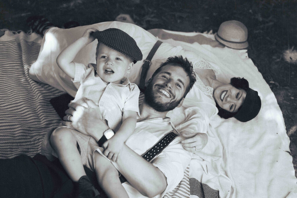 portait d'un couple et leur fils qui rient, couché sur une nappe de pique nique dans la nature