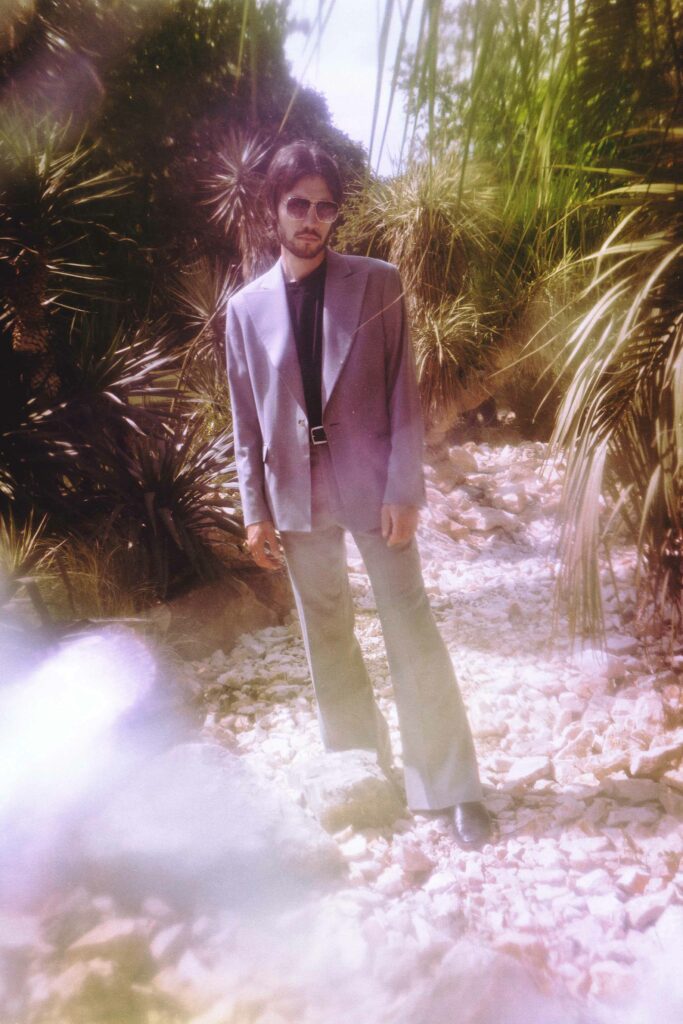 Portrait en pied d'un homme en costume qui se tient au milieu des palmiers, style nostalgique, mode années 70