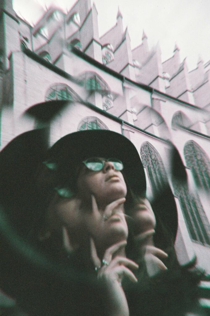 Portrait kaléidoscope d'une femme avec lunettes de soleil et chapeau, cathédrale en arrière-plan, style nostalgique pellicule argentique
