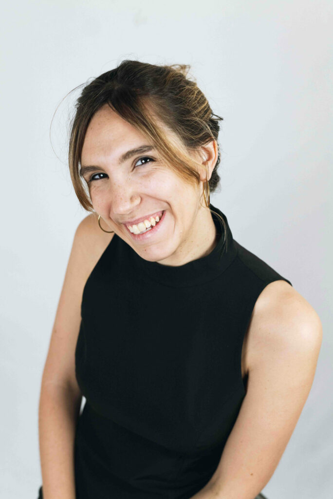 portrait d'une femme humoriste souriante vêtue d'un tailleur noir, style naturel et pro