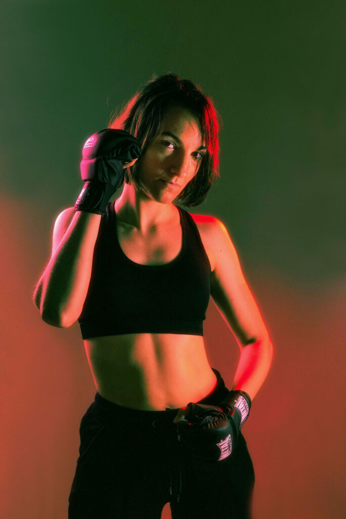 Portrait dynamique d’une femme sportive éclairée aux néons, portant des gants de boxe et un équipement de sport, énergie brute et détermination