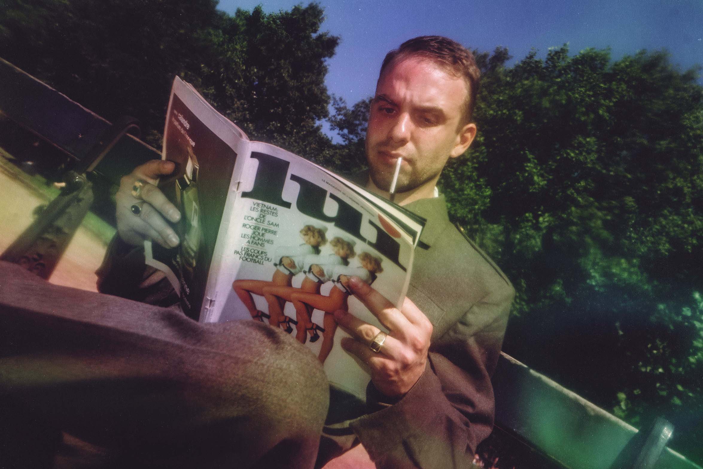 Photographie vintage d'un homme assis sur un banc, en veste militaire, lisant un magazine ancien.